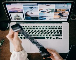 holding a camera films and a white laptop on the desk