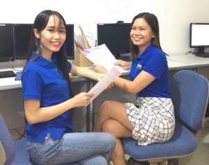 two female teachers with blue polo shirts sitting while holding a piece of paper